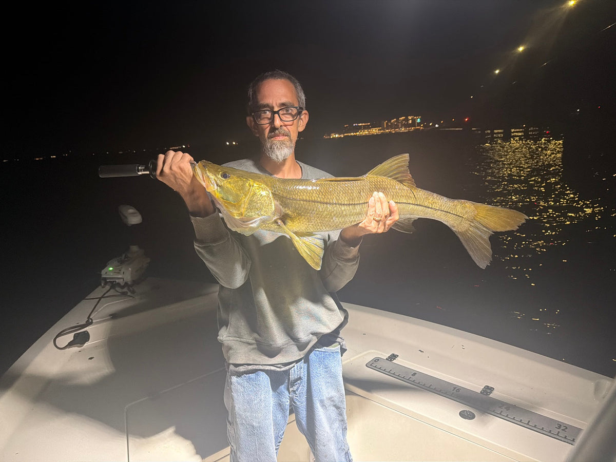 Angler holding a large snook at night on a boat in Southwest Florida